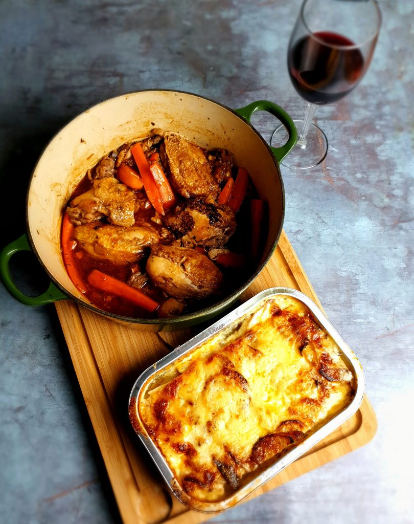 Takeaway food from Goodies Food Hall - showing a bowl of casserole, potatoes dauphinois and a glass of red wine