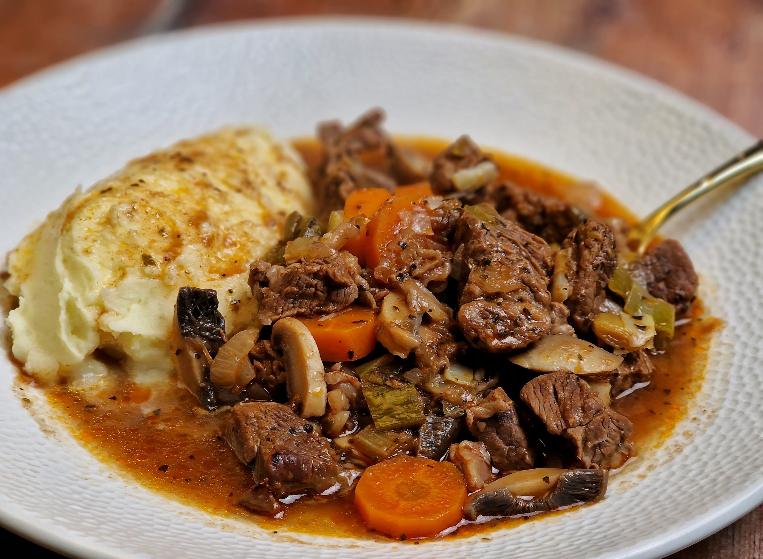 A bowl of beef and vegetable casserole with mashed potato